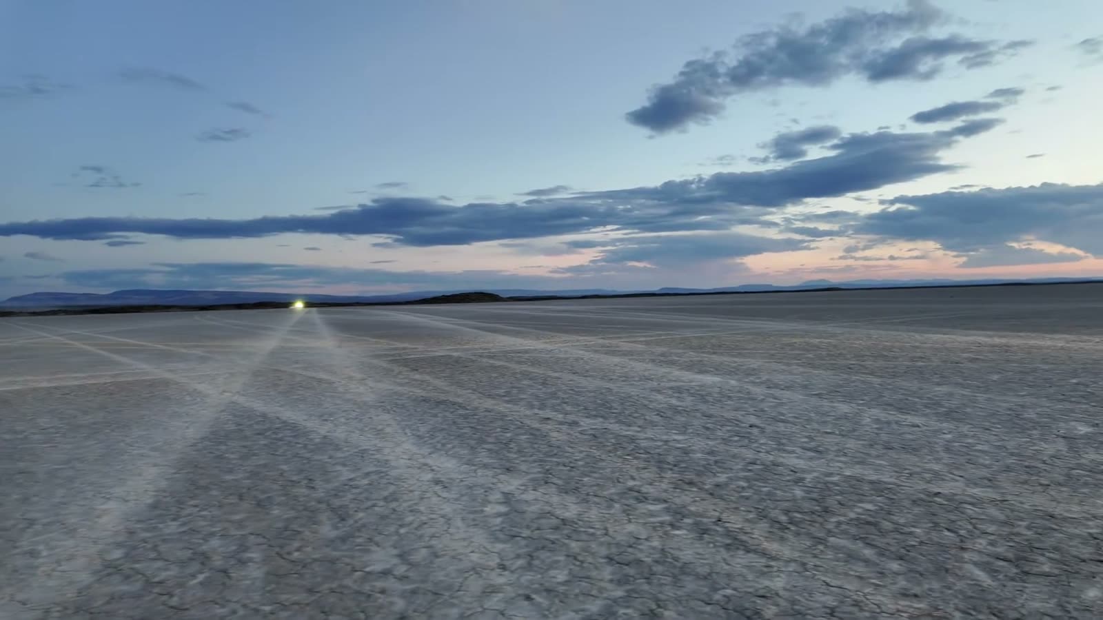 Headlights crossing the cracked surface of Coyote Lake at dusk