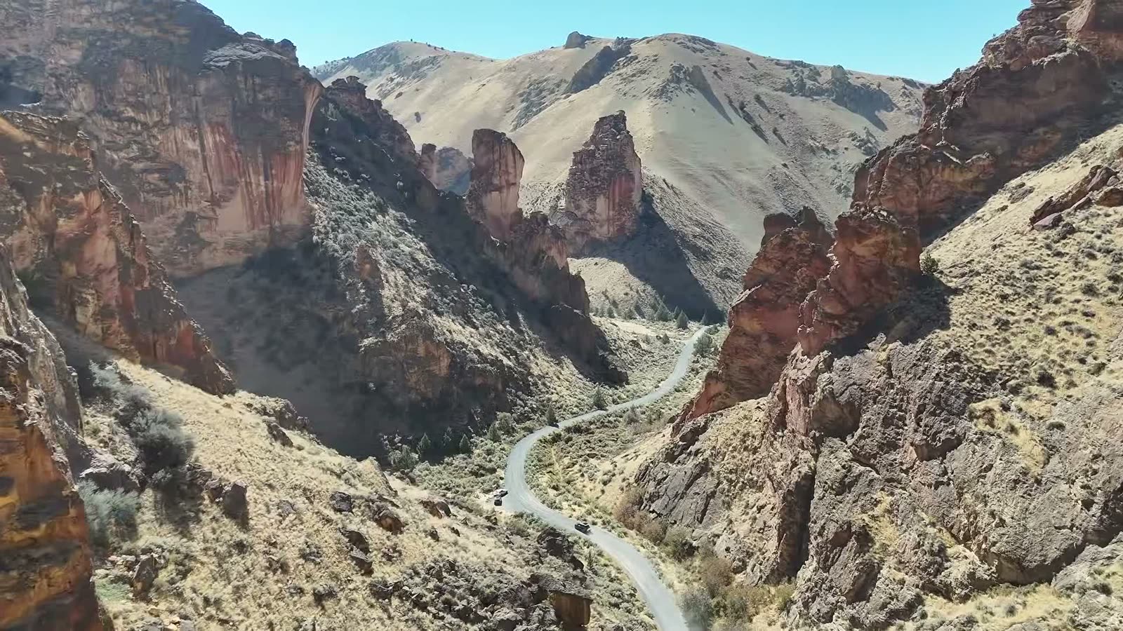 Red rock spires towering over the road through Leslie Gulch, with the convoy small on the road below